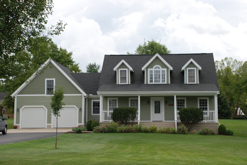 Gray Cape Cod house with three dormers, an attached garage and a wide lawn